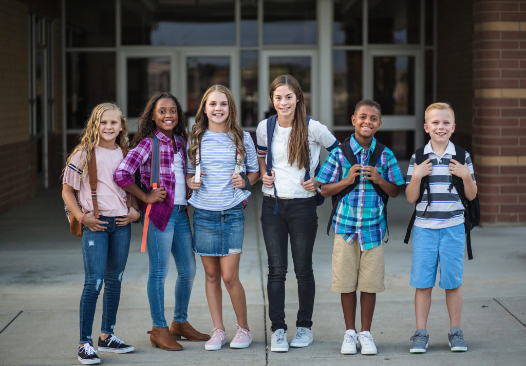 6 Children, boys and girls, standing outside of school with backpacks on