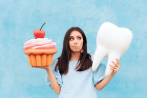 Woman holding cupcake, but looking at large tooth. Food that's bad for teeth.