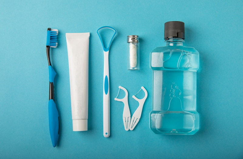 Toothbrush, tongue cleaner, dental floss, toothpaste tube and mouthwash on blue background with copy space. Flat lay. Dental hygiene.