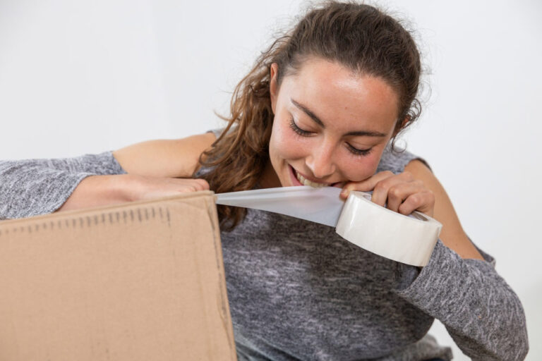 Young woman rips open packing tape with her teeth