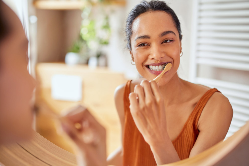 Smiling young woman brushes her teeth and looks in the mirror