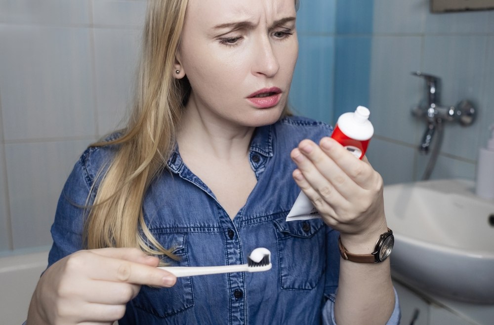 Woman examines tube of toothpaste confusedly looking for expiration date