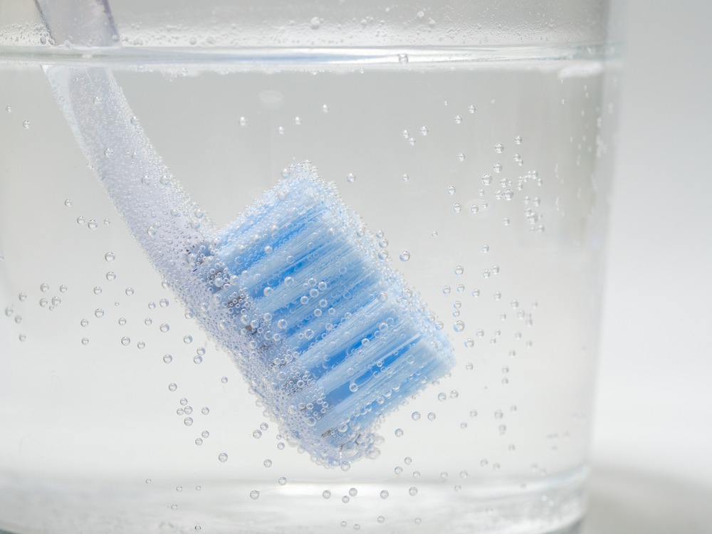 A manual toothbrush bristles down in a glass of bubbly disinfectant.