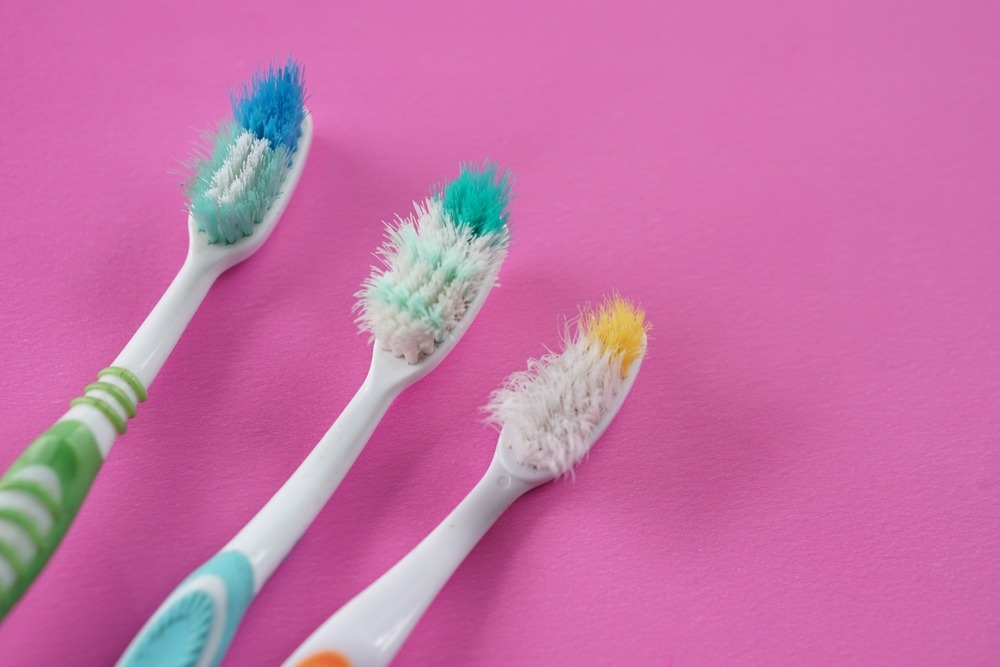 Three manual toothbrushes on a pink background, all showing signs of heavy use.